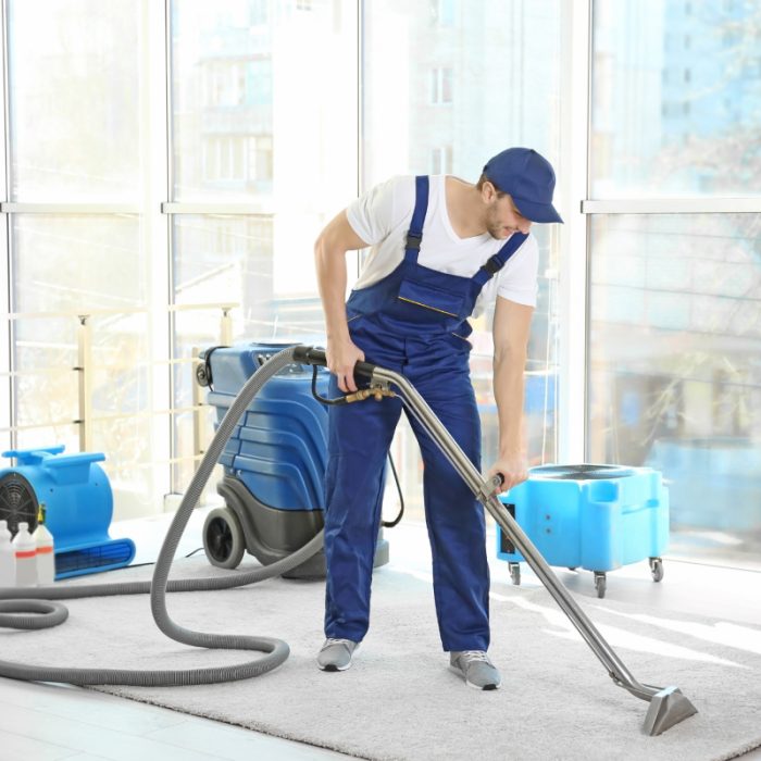 Man in bedrijfskleding reinigt vloer met industriële stofzuiger, voor thuis schoonmaken op aanvraag.